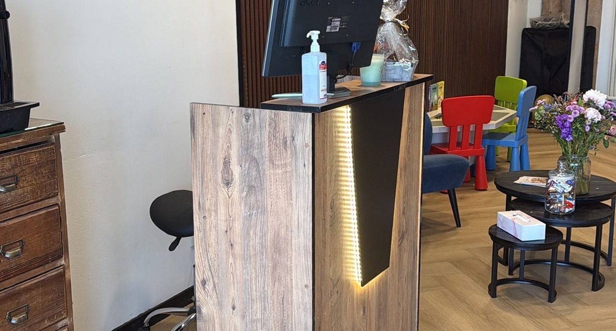 De houten balie met verlichting, met de speelhoek en bloemen erachter