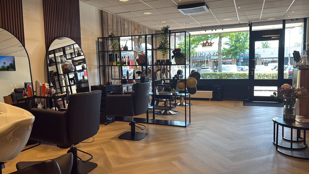 De salon in de lengte: kappersstoelen, gebogen spiegels en de ramen aan de straat