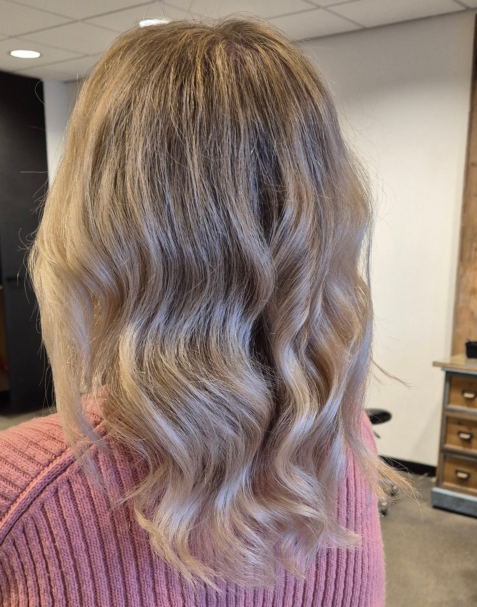 Blonde golvende balayage boven een roze trui